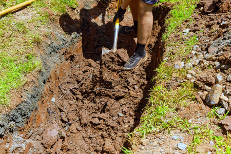 Worker digs trench for drainage pipe with shovelの写真素材