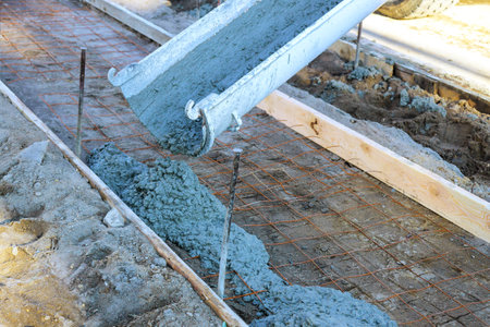 Concrete mixer truck pours fresh concrete on reinforced bars in preparation for new sidewalkの写真素材