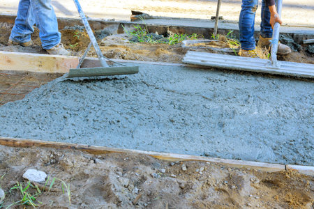Worker using trowel leveling concrete during freshly cement pouring of sidewalkの写真素材