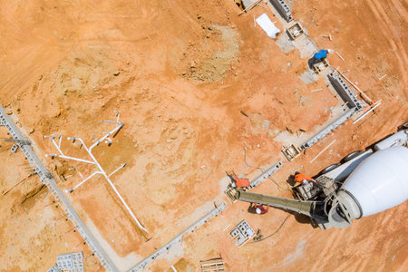 Concrete mixer truck being used by construction worker as it pours concrete along foundation in an...