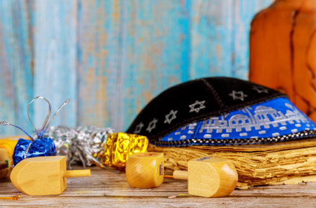 Colorful dreidels chocolate gelt rest on wooden table, accompanied by traditional kippah, creating festive atmosphere for Hanukkah celebrations.の写真素材