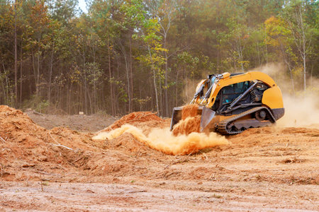 Powerful bulldozer is actively pushing dirt debris at construction site surrounded by trees dust clouds billow into air as land is being prepared for development.の写真素材