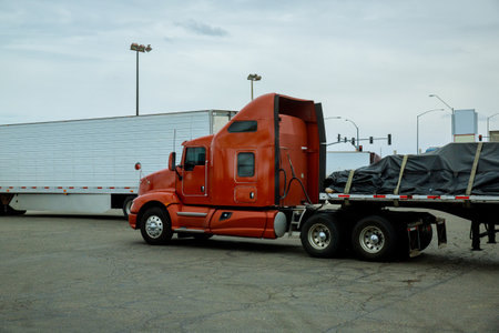 Semi truck with high cab is parked beside white trailer in busy parking lot.の写真素材