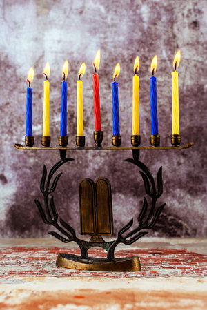 Beautifully crafted menorah stands with eight lit candles, featuring blue, yellow, one red candle,...