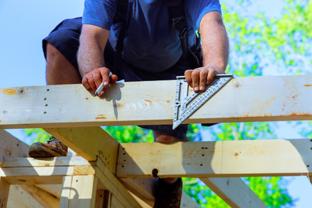 Carpenter uses square tool to measure wood frame beams while working on under construction project at work areaの写真素材