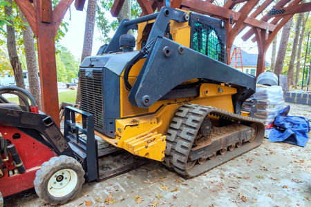 Tracked loader rests beside wooden pavilion surrounded by trees in during construction framework...