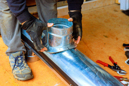 Skilled worker installs metal duct fitting, ensuring secure connection for HVAC heating ventilation...