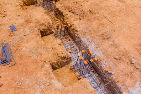 Workers are preparing concrete foundation in an urban construction site with metal rebar, gravel...
