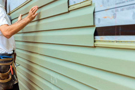Construction worker carefully aligns, installs green pvc siding board on exterior of house in during renovation project.の写真素材