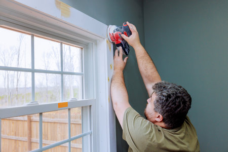 Skilled worker is sanding wooden window trim, preparing for painting in home improvement effort.の写真素材
