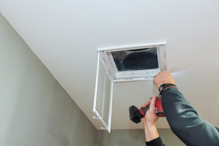 Technician secures ventilation cover in newly renovated ceiling, during home renovation improvementの写真素材