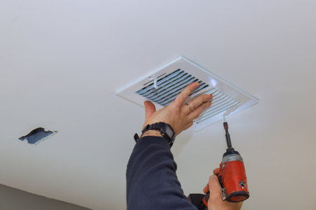 Contractor is using drill to install ceiling vent in living room setting.の写真素材