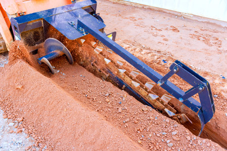 Trencher machinery is actively digging into earth at construction site