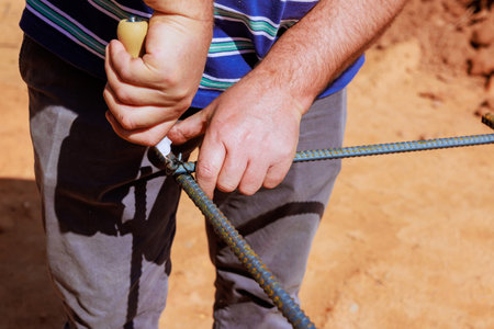 Construction worker carefully secures steel rebar with knot in busy outdoor setting during work day.