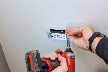 Individual works on installing wall outlet featuring USB ports, utilizing power drill for task.
