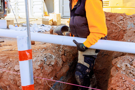 Worker carefully cutting plumbing pvc pipes in trench to sewer lines system at construction siteの写真素材