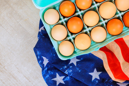 Turquoise egg carton filled with brown, orange eggs positioned on folded American flag featuring...