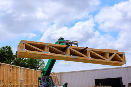 Construction workers operate telehandler crane to raise large wooden beams at building site under...