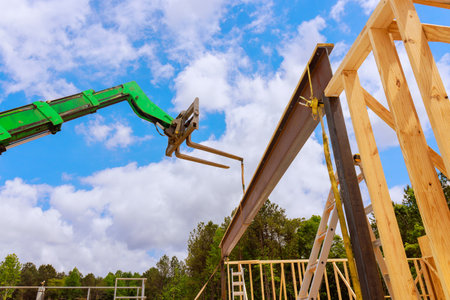 Telehandler construction crane is lifting steel beam into position at wooden frame