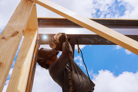Construction worker uses welding tool to assemble metal beam frame in works day