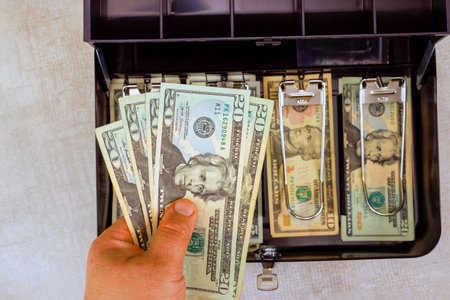 Hand with American dollars banknotes shows money management in cash box filled with various...