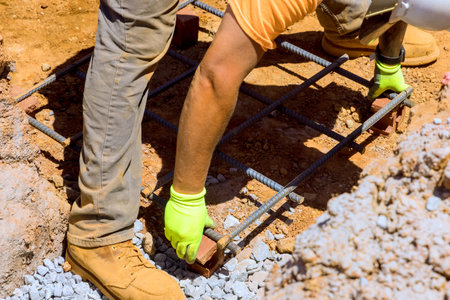 Construction worker sets up rebar framework on gravel ground at construction site in ensuring...
