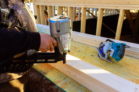 Contractor worker applies nail gun to wooden beams while working on construction projectの写真素材