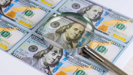 Magnifying glass highlights details of US hundred dollar bill featuring Benjamin Franklin.の写真素材