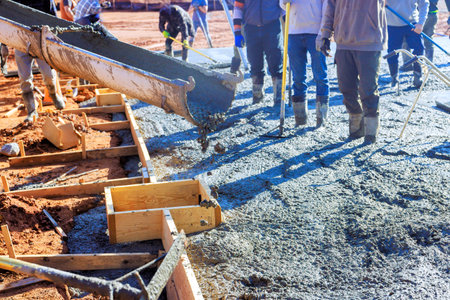 Workers are pouring fresh concrete into wooden forms at construction site