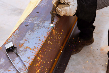 Skilled worker cuts steel beam, producing bright sparks in construction site using through