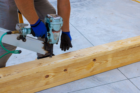 Craftsman focuses on nailing wooden beams together at construction site using pneumatic nail gun