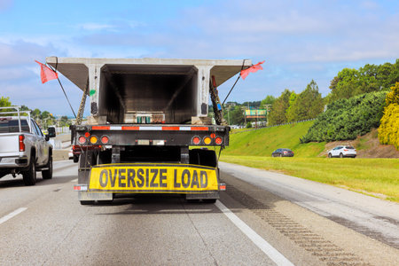 Large truck equipped with an oversize load sign drives along busy highway under transportation in motion.の写真素材