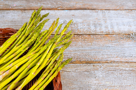 Freshly harvested organic asparagus vibrant green colors in wicker basket, resting on weathered wooden table.の写真素材