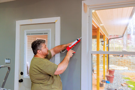 Carpenter carefully seals gaps around windows with caulk while renovating room in house.の写真素材