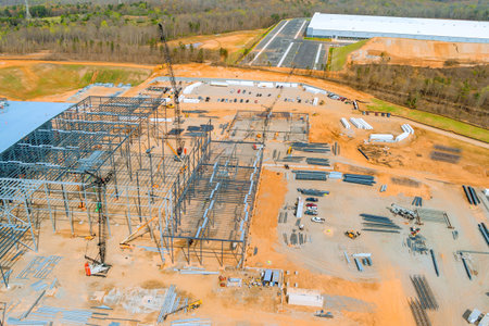Construction workers operate cranes machinery to build large facility in works location under metal...