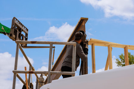 Skilled worker welding metal beam framing on building site while operating machinery under works dayの写真素材