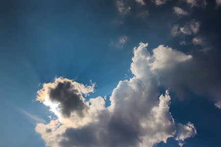 Sunlight filters through fluffy clouds, creating serene atmosphere in afternoon sky.の写真素材