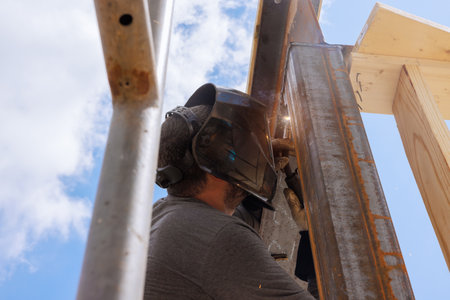 Skilled welder focuses on metal beam structure using protective gear while working outdoors