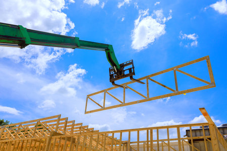 Forklift telehandler crane lifts large wooden truss into place, helping to construct new home under...