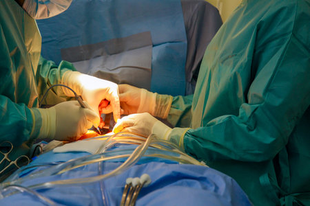 Two surgeons, one man and one woman, focus intently on surgery in hospital operating room. Medical...