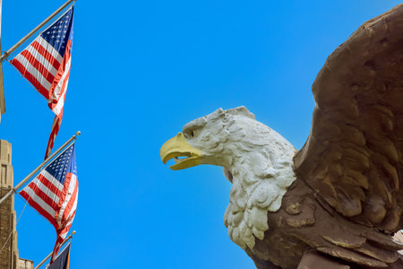 Eagle sculpture towers over American flags, creating patriotic atmosphere in an urban settingの写真素材