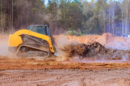 Bulldozer works diligently to clear debris from wooded land, dust smoke rising in construction siteの写真素材