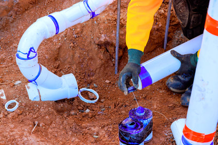 Worker connects new plumbing sewage pipes while fixing drainage system in residential yard during work dayの写真素材