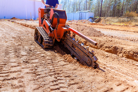 Heavy trenching machinery digs trench in soil for construction purposes on work siteの写真素材