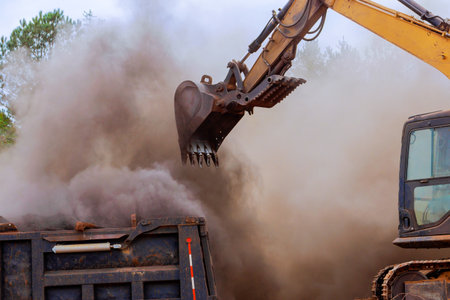 Heavy machinery operates to load construction debris into truck, creating cloud of dust at works site.の写真素材
