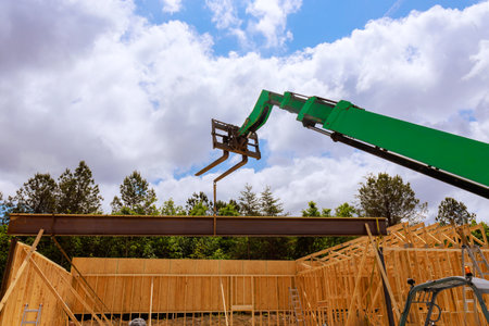 Construction crew uses telehandler crane to hoist steel beam into place near wooden frame structure