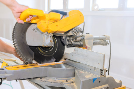 Contractor carefully uses miter saw to cut wood in well lit workshop, on accuracy craftsmanship.の写真素材