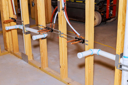 Copper, PVC pipes are being installed along wooden framing in basement, in plumbing setup process.