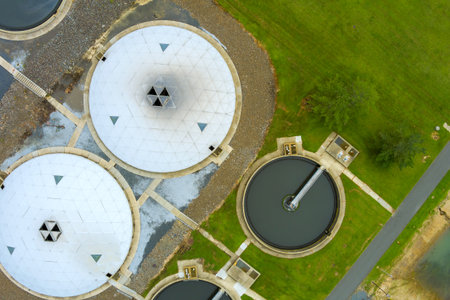 Circular tanks at wastewater treatment facility are surrounded by grassy areas, highlighting urban...
