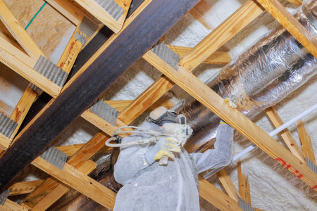 Construction worker is installing thermal barrier insulation in an attic with spray equipment to improve energy efficiency.の写真素材